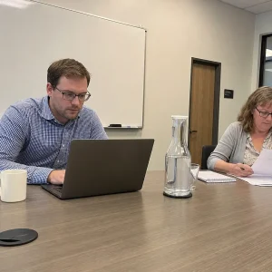 Konsult och kommunanställd arbetar tillsammans vid ett konferensbord med laptop och dokument under ett möte om kommun it-b...