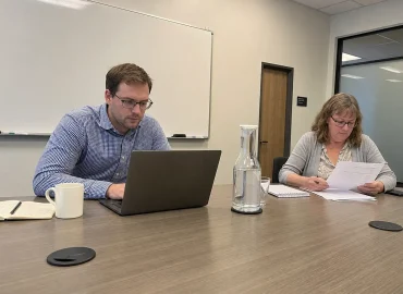 Konsult och kommunanställd arbetar tillsammans vid ett konferensbord med laptop och dokument under ett möte om kommun it-b...